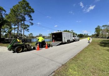 Mowing crew loading equipment beside a road with a trailer and safety cones on a sunny day